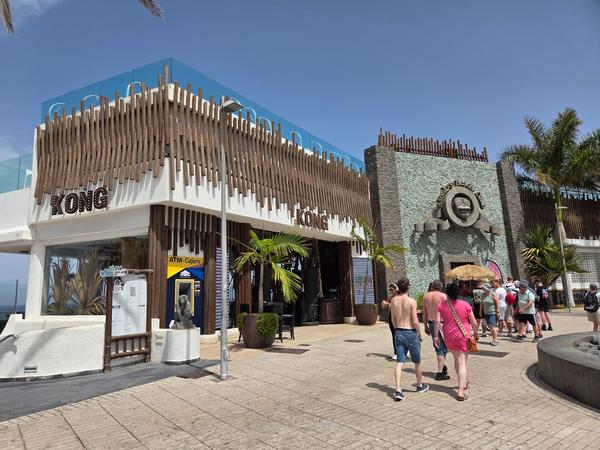 Fachada del Monkey Beach Club en Tenerife, con diseño moderno y turistas caminando cerca de la entrada.
