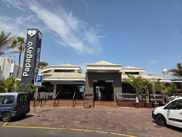 Exterior del club Papagayo en Tenerife, con palmeras y letrero vertical distintivo.