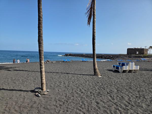 Playa Jardín, Tenerife Vista de Playa Jardín en Puerto de la Cruz con arena negra, palmeras y el castillo al fondo.