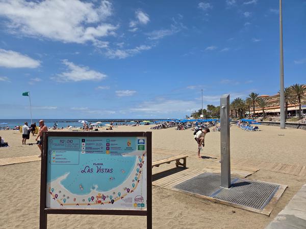 Playa de Las Vistas en Arona Vista general de la Playa de Las Vistas en Tenerife, con cartel informativo, duchas y turistas disfrutando del sol.