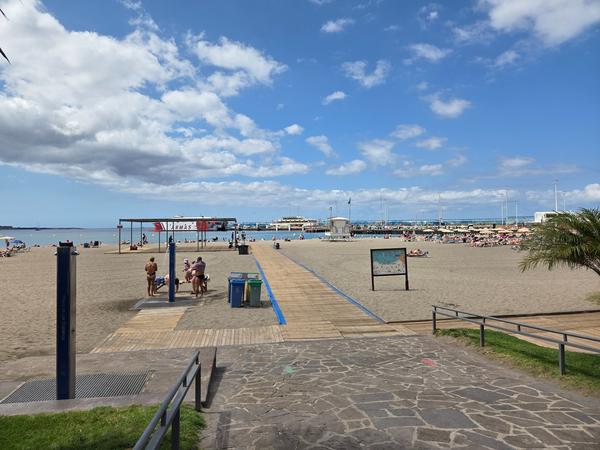 Playa de Los Cristianos Playa de Los Cristianos con pasarela de madera, duchas, sombrillas y fondo de puerto con barco de Armas.