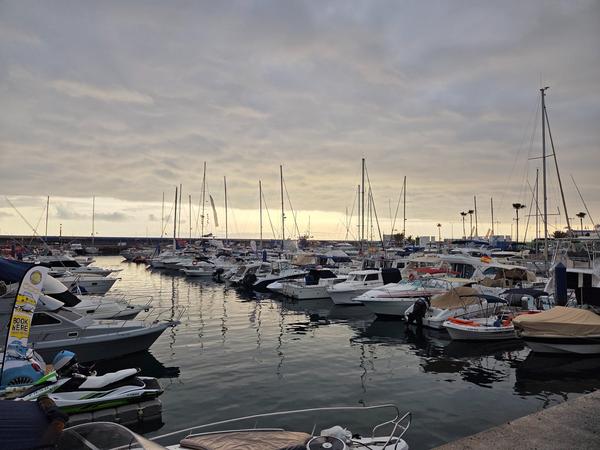 Puerto Colón en Tenerife al atardecer, con numerosos barcos y yates atracados bajo un cielo nublado.