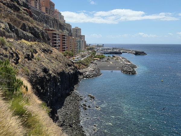 Vista de Radazul desde el sendero Vista panorámica del litoral de Radazul con edificios junto a los acantilados y una playa urbana de arena oscura.