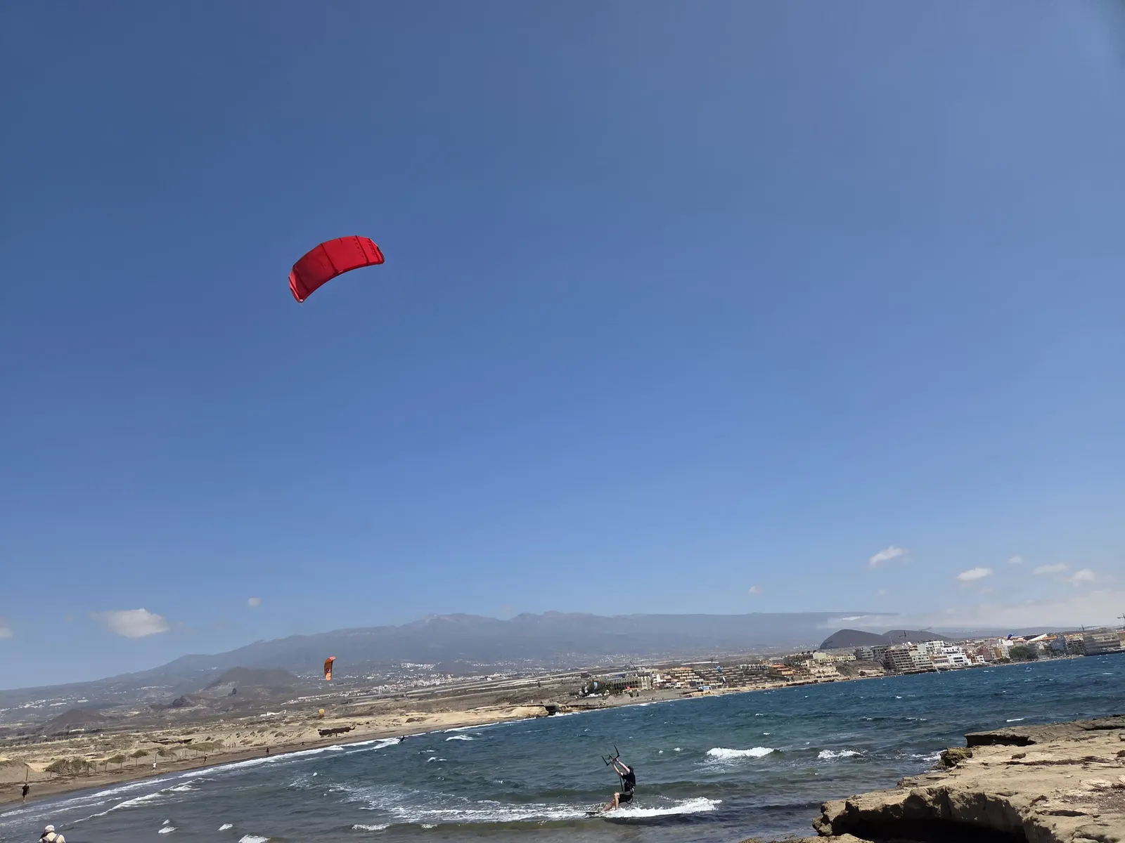 Kitesurfista navegando con una cometa roja frente a la costa rocosa de El Médano