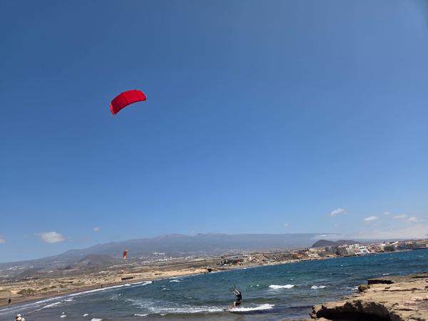 Persona practicando kitesurf con cometa roja sobre el mar en El Médano, Tenerife.