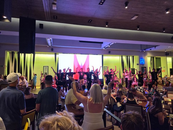 Actuación musical en el interior de Hard Rock Cafe, con varios artistas sobre el escenario y el público participando con los brazos levantados.
