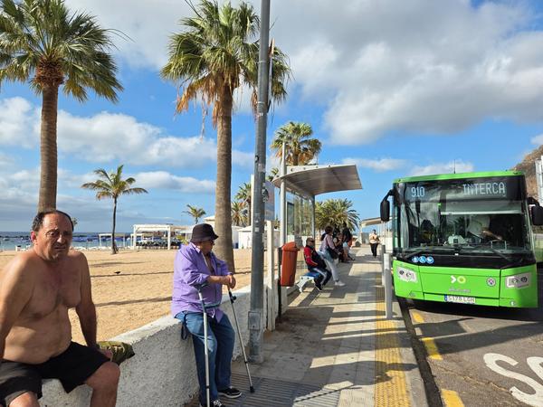 Parada de autobús junto a la playa de Las Teresitas con guagua verde de la línea 910 y turistas esperando.