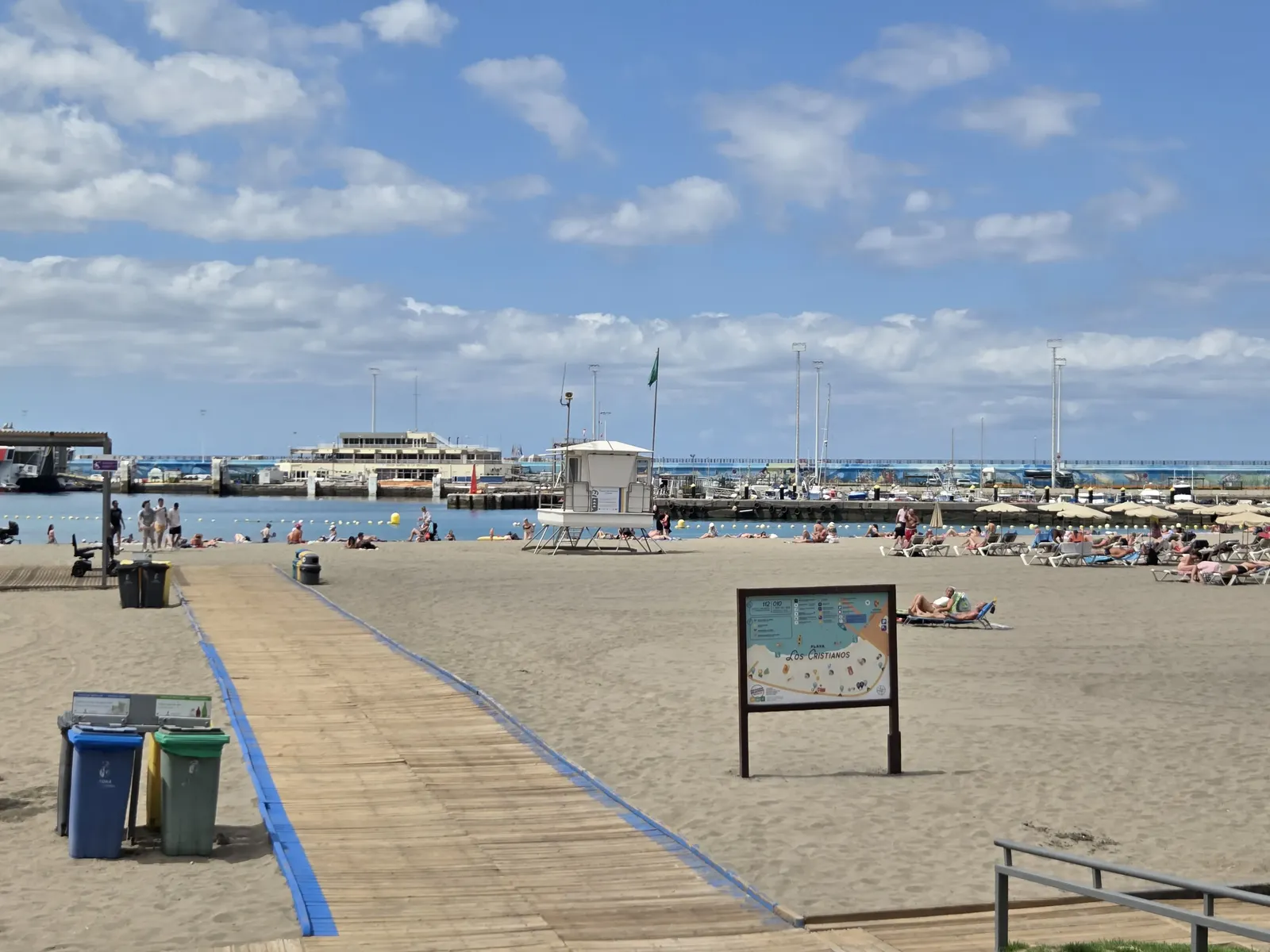 Playa de arena clara de Los Cristianos con el puerto y sus veleros al fondo