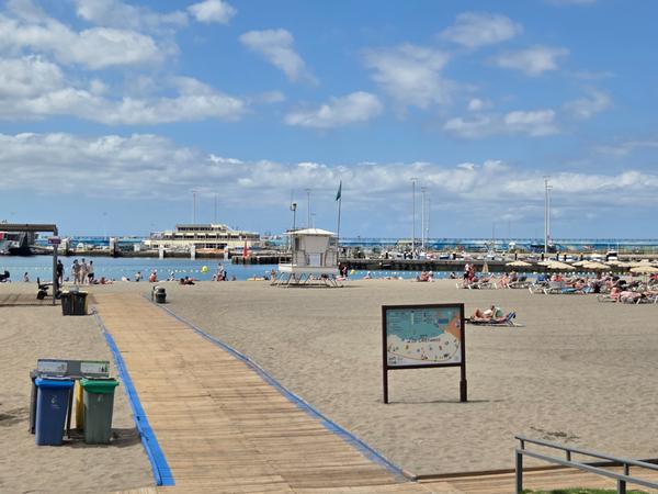 Playa de Los Cristianos con turistas tomando el sol frente al puerto deportivo en un día soleado.