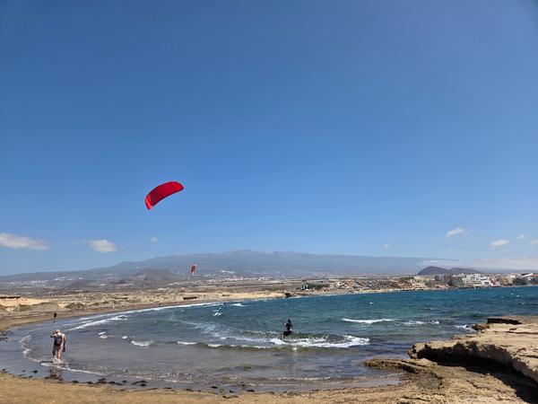 Kitesurf en El Médano Persona practicando kitesurf en El Médano, Tenerife, con cometas y el Teide al fondo.