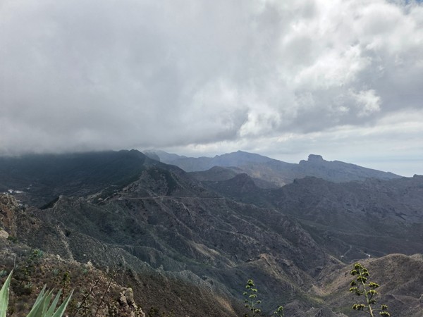 Paisaje montañoso y volcánico de Tenerife bajo un cielo cubierto, con crestas escarpadas y una carretera que cruza la ladera.