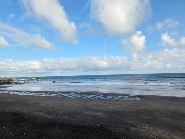 Playa de Almáciga, Tenerife Playa de Almáciga en Tenerife con arena oscura, formaciones rocosas y cielo parcialmente nublado sobre el océano Atlántico.