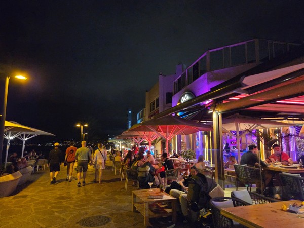 Paseo nocturno en Playa de las Américas con terrazas iluminadas, personas caminando junto al mar y ambiente animado en la zona de restaurantes.