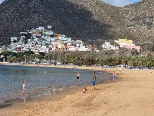 Playa de Las Teresitas con vista a San Andrés Personas disfrutando de la Playa de Las Teresitas con casas de colores al fondo en la montaña.