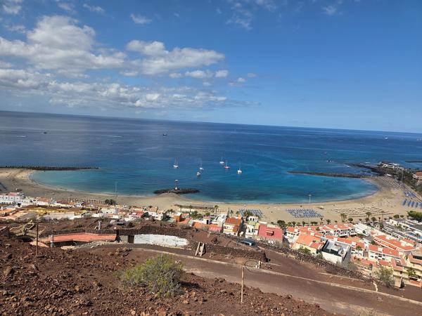 Vista elevada de Playa de Las Vistas con su forma curvada, rompeolas y barcos anclados en el mar.