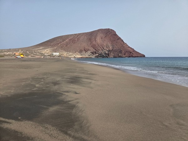 Playa de La Tejita con arena amplia, mar tranquilo y la Montaña Roja destacando junto a la costa.