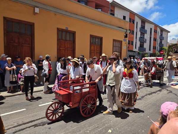 Desfile festivo en una calle con personas vestidas con trajes tradicionales y carretas de madera durante una celebración popular.